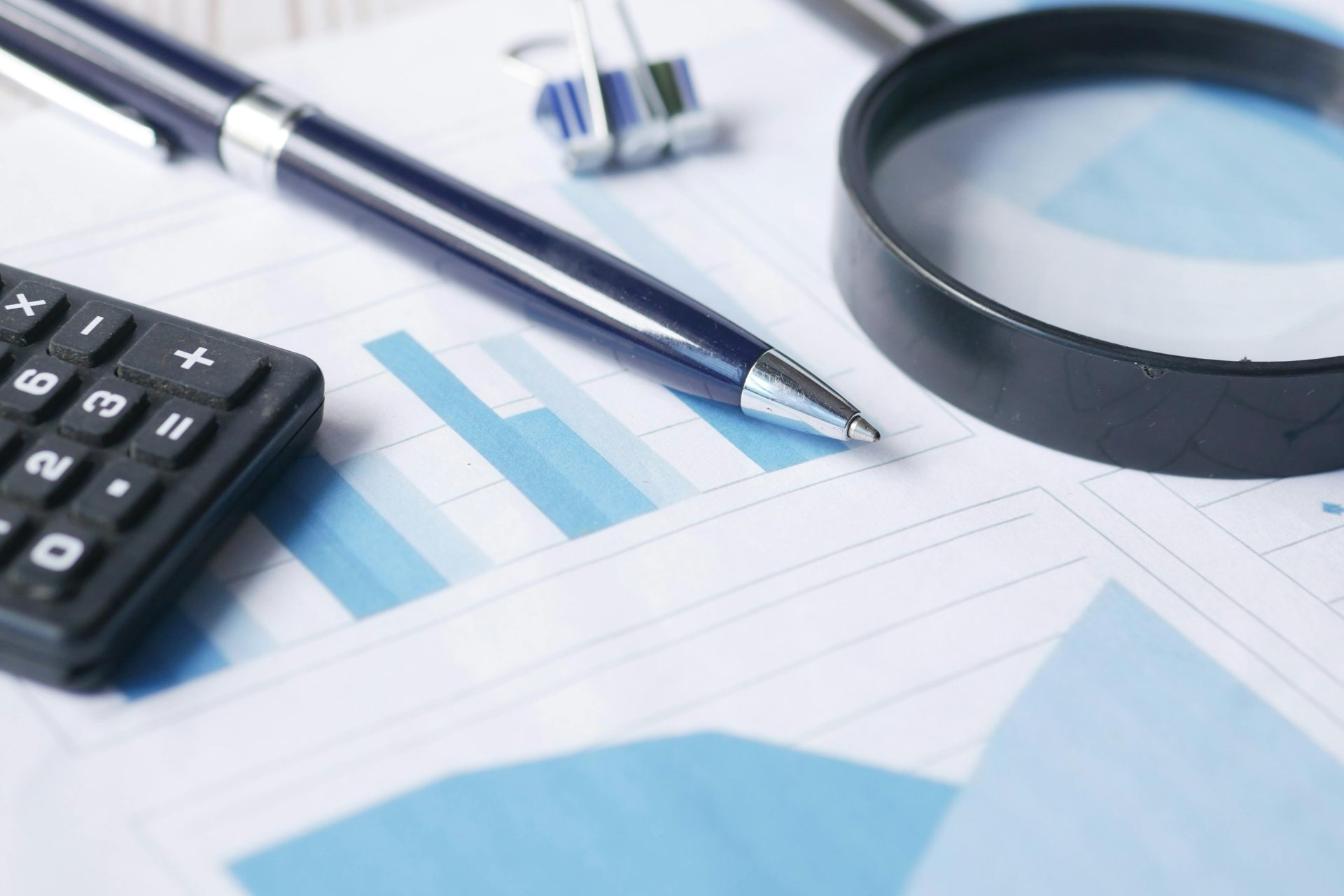Gros plan sur une calculatrice, un stylo et une loupe sur des documents financiers.