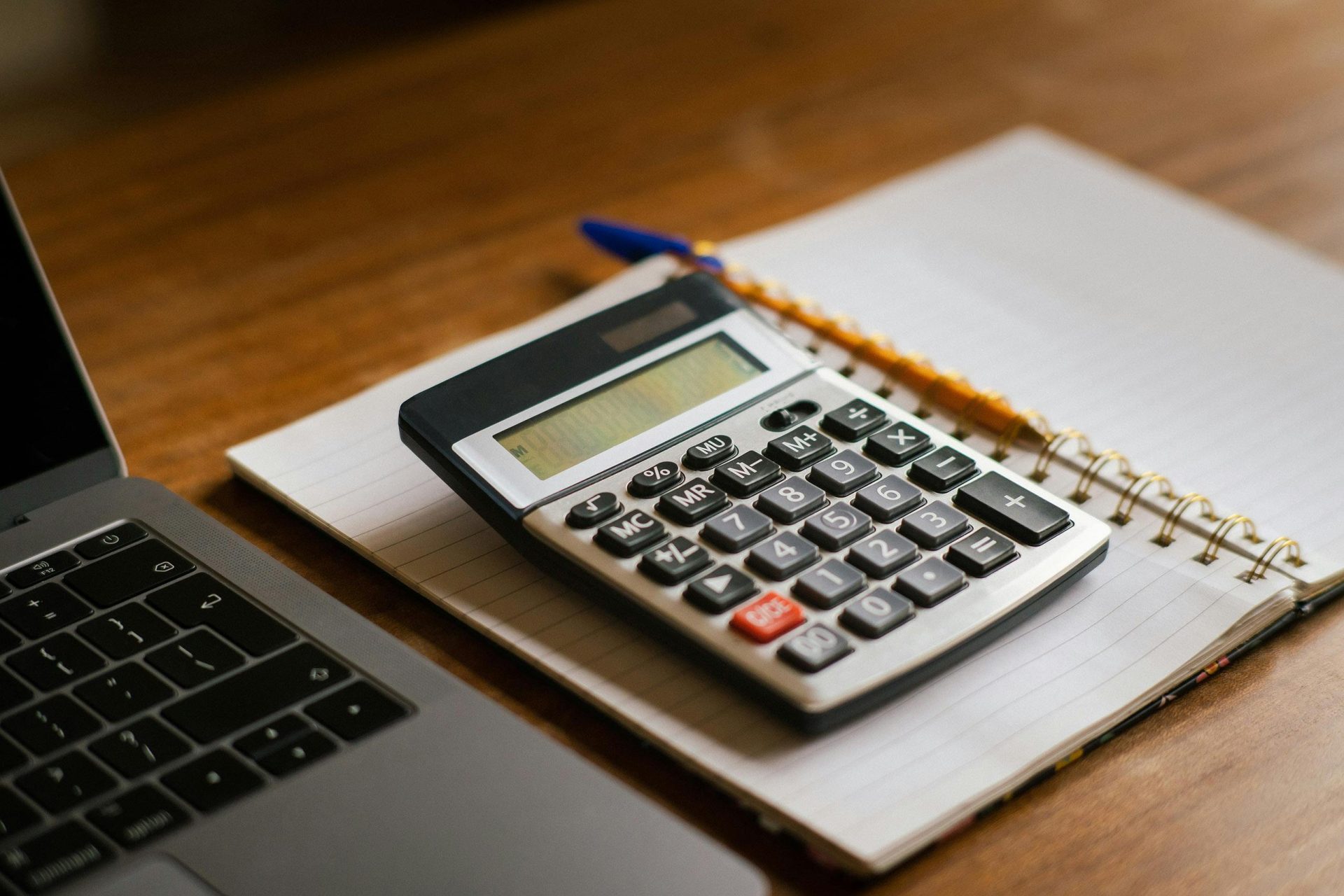 Calculatrice et ordinateur portable ouvert sur un bureau en bois, idéal pour les tâches financières ou comptables.